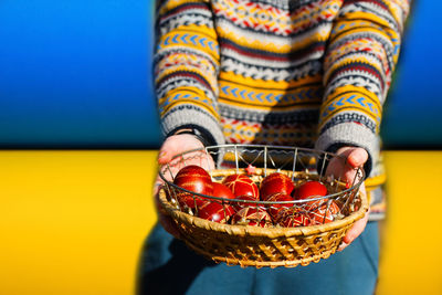 Ukrainian young smiling woman in hat holding plate of collection of red egg on nature background. 