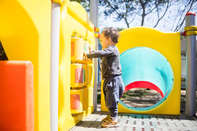 Toddler boy plays on colorful children playground at the park.