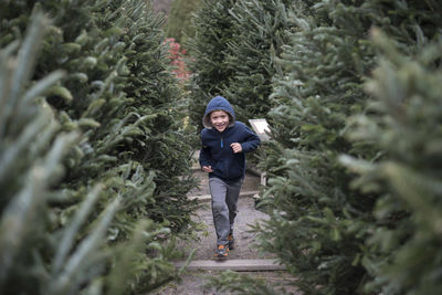 Portrait of happy boy running by pine trees in farm