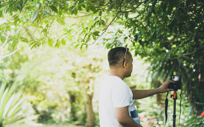 Side view of young man standing against trees