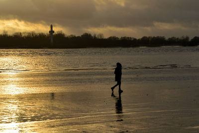 Silhouette man standing on beach against sky during sunset