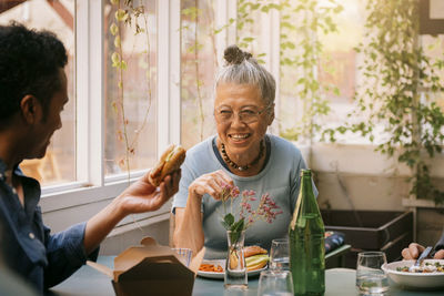 Happy senior woman enjoying food with male friend while sitting at restaurant