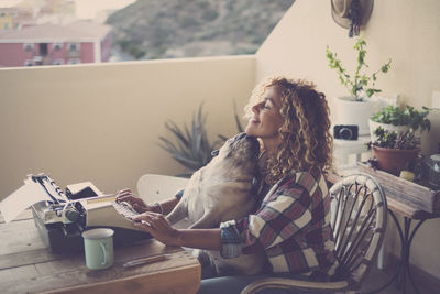 Woman using typewriter while sitting with dog in balcony