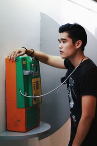 Young man using mobile phone while standing against wall