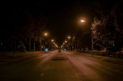 Empty road along illuminated trees at night