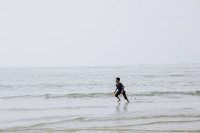 Boy running in sea against sky