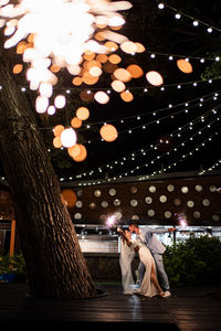 Woman standing by illuminated tree at night