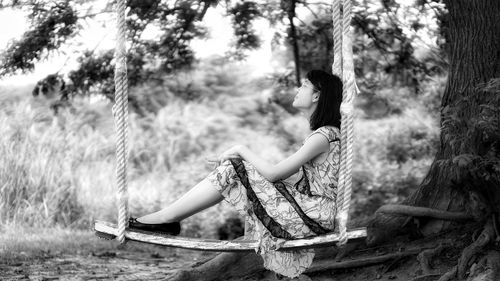 Side view of woman sitting on tree trunk in forest