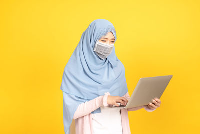 Mid adult man using mobile phone against yellow background