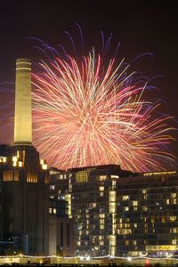Firework display in city against sky at night