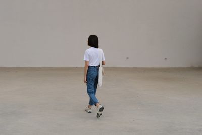 Rear view full length of woman walking on floor against wall