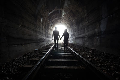Silhouette people walking on railroad track tunnel