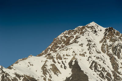 Low angle view of snowcapped mountains against clear blue sky