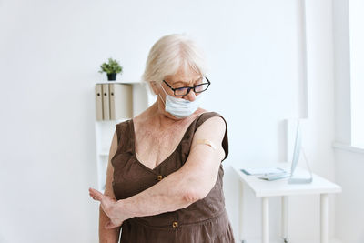 Senior woman wearing mask looking at bandage