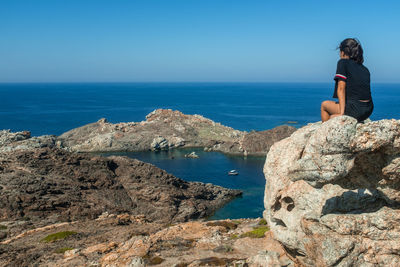 Rear view of a teenage girl sitting on the rocks of the cap de creus headland in catalonia, spain. 