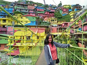 Portrait of smiling young woman standing against buildings