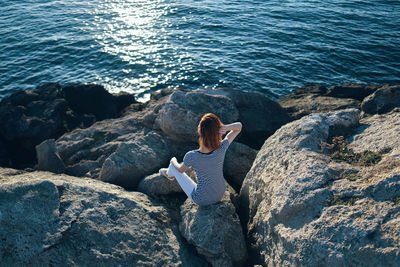 Rear view of woman sitting on rock by sea