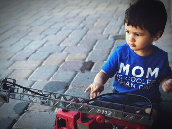 Cute boy playing with toy crane on footpath