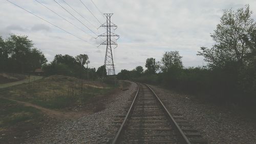 Railroad track by electricity pylon against sky