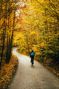 Rear view of woman riding bicycle on footpath during autumn