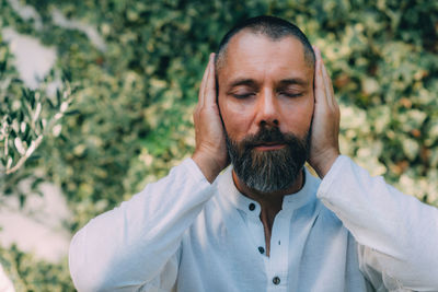 Man sitting with his eyes closed and doing a reiki auto treatment, holding hands on ears.