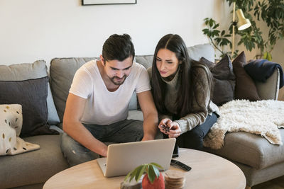 Couple using credit card while shopping online through laptop on sofa at home