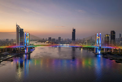 Illuminated bridge over river against sky at sunset
