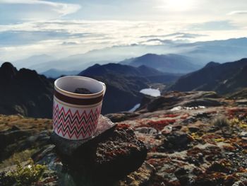 Coffee cup on rock by mountains against sky