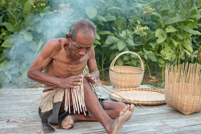 Shirtless senior man making straw basket