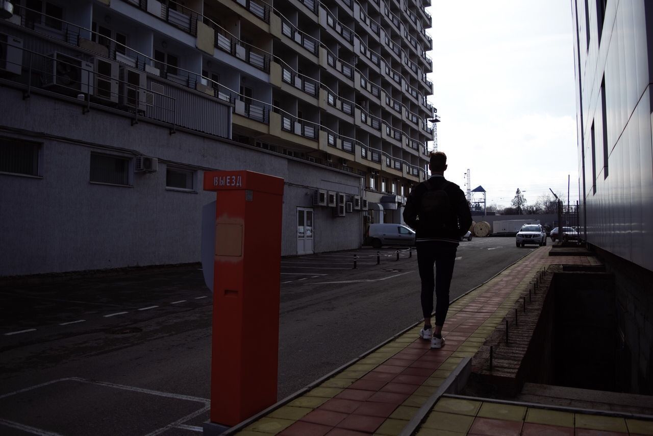 REAR VIEW OF MAN WALKING ON STREET BY BUILDINGS