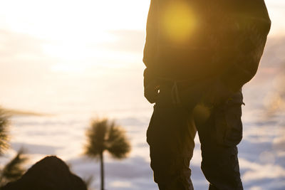 Low section of woman walking on beach against sky during sunset