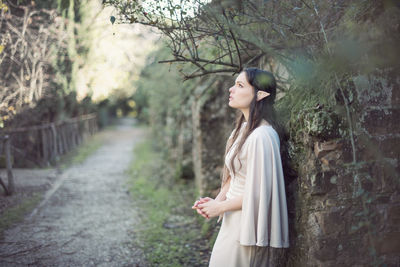 Side view of young woman standing against trees