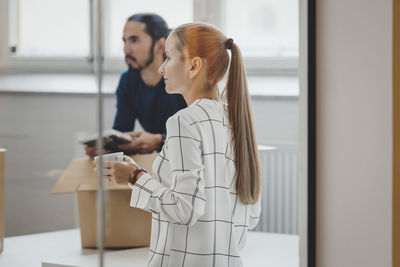 Mid adult businesswoman holding coffee cup while male colleague in background at new office