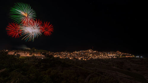 Firework display in town against sky at night