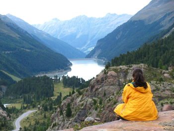 Rear view of woman sitting on rock by mountains
