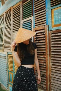 Woman wearing hat while standing by wooden wall