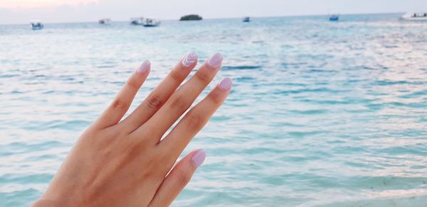 Cropped image of woman hand with nail polish on fingernails against sea