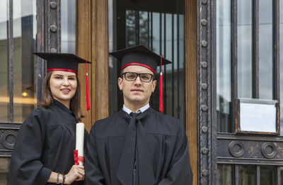 Portrait of couple wearing graduation gowns standing by door