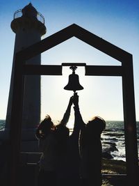 Girls holding bell by lighthouse against sky