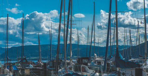 Boats moored at harbor against cloudy sky