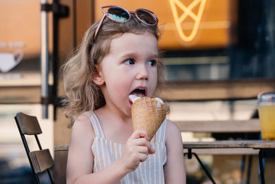 Toddler child eating cone ice cream outside near cafe. cute blonde caucasian girl licking frozen