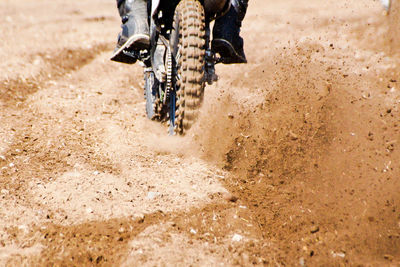 Low section of person riding motorcycle on dirt road