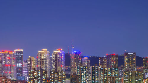 Illuminated cityscape against clear blue sky