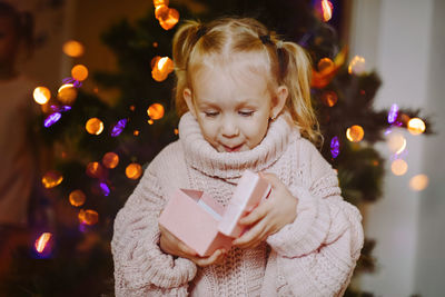 Cheerful baby girl with a gift box on the background of festive christmas tree on new year's eve