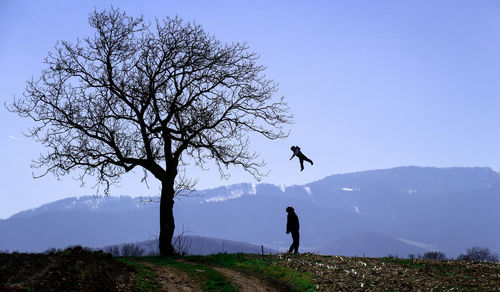 Silhouette man catching son by tree against sky