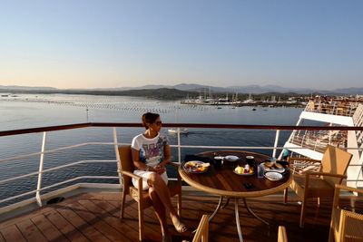 Man sitting on table by sea against clear sky