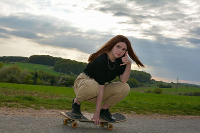 Full length of young woman sitting on a skateboard against sky