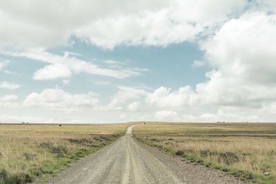 Empty road amidst field against sky