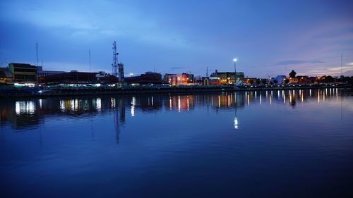 Illuminated buildings by river against sky at dusk