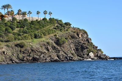 Rock formation by sea against clear blue sky